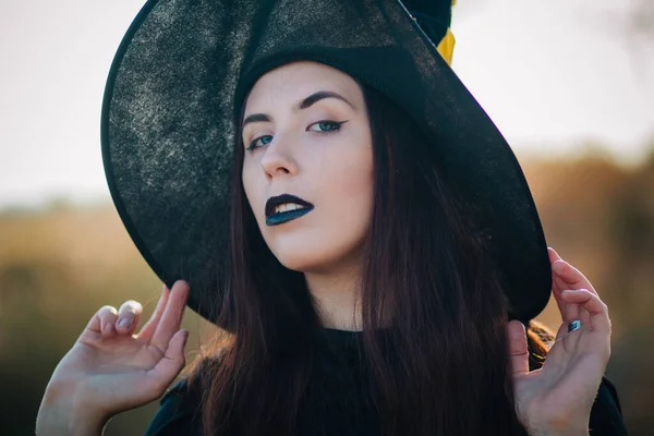 一个有着苍白皮肤和黑色嘴唇戴着大大的黑色帽子的漂亮女孩的画像 万圣节的女巫形象中的女人 — 图库照片