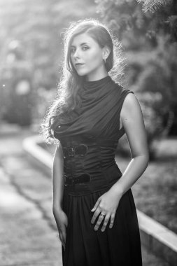 Güzel, siyah elbiseli, korseli genç bir kadın akşam vakti parkta yürüyor..