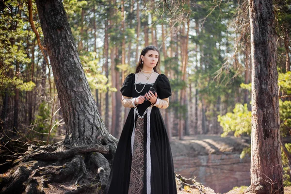 身穿中世纪黑色连衣裙 身披钢铁的年轻貌美的女人手牵着手在森林里走着 穿着哥特式衣服的迷人女孩 — 图库照片