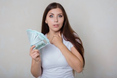 Beyaz tişörtlü, genç, güzel bir kadın. Elinde para, beyaz bir arka planda izole edilmiş..