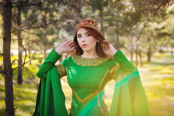 一个漂亮的 年轻的 红头发的姑娘 穿着中世纪绿色的连衣裙 袖子很长 头戴金色的皇冠 站在草地上 在仙境中 太神奇了 皮肤洁白的模特 — 图库照片