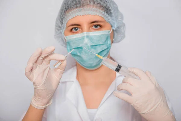 身穿白衣 头戴医疗帽 戴口罩和手套的女医生与注射针和医疗座便器一起工作 一位穿着无菌衣服的科学家站在白底上准备了疫苗 Coronavirus疫苗搜索概念 — 图库照片