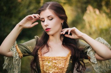 Parkta dolaşan yeşil rokoko elbiseli çekici genç bir kadının portresi. Temiz ciltli bir model.