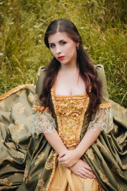 Yeşil rokoko elbiseli güzel bir kadın çimlerin üzerinde otururken poz veriyor. Yakın plan portre. Temiz ciltli bir model..