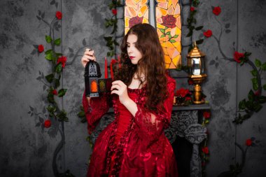 Rococo döneminin muhteşem kırmızı elbiseli güzel bir kız elinde mumlarla bir şömine, bir pencere ve çiçeklerin karşısında duruyor..