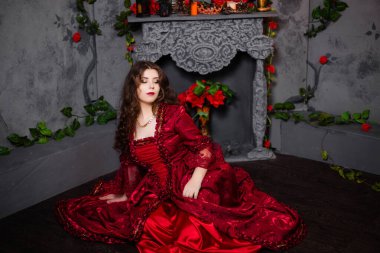 Rococo döneminin muhteşem kırmızı elbiseli güzel bir kız şöminenin yanında oturuyor ve çiçekler..