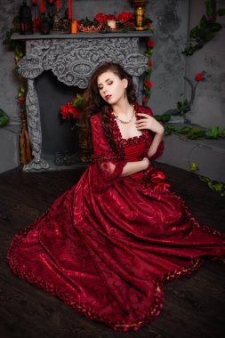 Rococo döneminin muhteşem kırmızı elbiseli güzel bir kız şöminenin yanında oturuyor ve çiçekler..