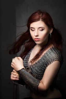 Elinde kılıçla zincirli güzel bir savaşçı kız. Ortaçağ fantazisi Valkyrie uzun saçlı koyu bir arka planda poz veriyor..