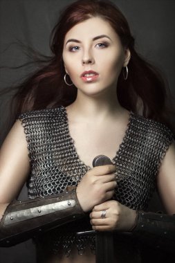 Elinde kılıçla zincirli güzel bir savaşçı kız. Ortaçağ fantazisi Valkyrie uzun saçlı koyu bir arka planda poz veriyor..
