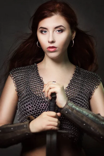 Beautiful girl warrior in chain mail with a sword in his hands. Medieval fantasy valkyrie with long hair posing on a dark background.