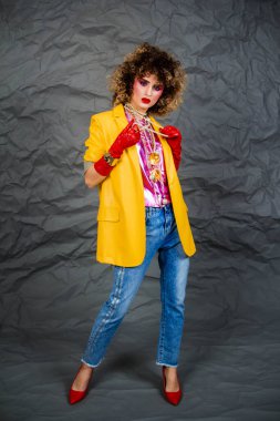 Sarı ceketli, mavi kotlu, afro saçlı bir kız. 80 'lerin modası, disko çağı. Gri arkaplanda stüdyo fotoğrafı.