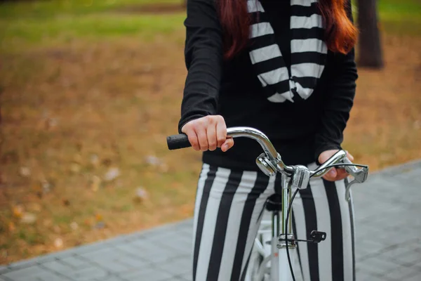 Close up of female hands on a bicycle handlebar on a background of an autumn park.