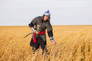 Doğulu bir savaşçı kılıçlı ve miğferli. 16. ve 18. yüzyıldan kalma. Buğday tarlasında dizlerine kadar duruyor..