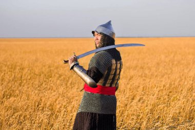 Doğulu bir savaşçı kılıçlı ve miğferli. 16. ve 18. yüzyıldan kalma. Buğday tarlasında dizlerine kadar duruyor..