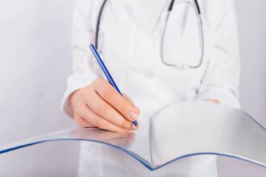 Beyaz önlüklü bir doktorun elleri bir klasör tutuyor ve beyaz bir arkaplanda izole edilmiş tıbbi bir belge dolduruyor..