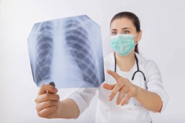 Bir doktorun ellerinde kaburga ve akciğer röntgeni. Boynunda steteskop olan beyaz önlüklü bir kadın florografi okuyor..