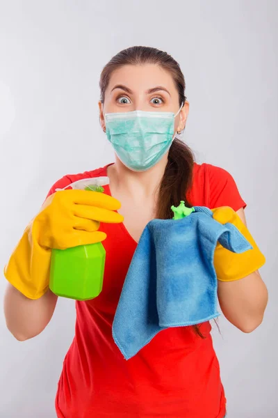 A young woman in a mask and gloves holds a spray bottle and a rag with a model of coronavirus. Concept art for cleaning the premises and the prevention of viral diseases.