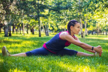 Spor yapan kadın bacaklarını esnetme egzersizleri yapıyor, bacaklarını ayırıyor. Bahçedeki parkta..