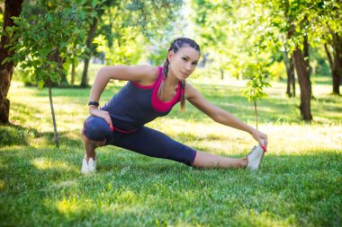 Spor yapan kadın bacaklarını esnetme egzersizleri yapıyor, bacaklarını ayırıyor. Bahçedeki parkta..