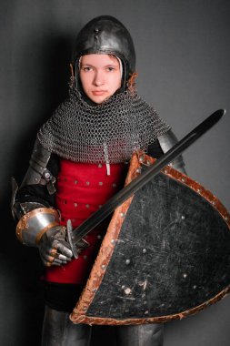 Ortaçağ zırhlı genç bir şövalye. Gri bir arka planda duran kılıç ve kalkanla donatılmış..