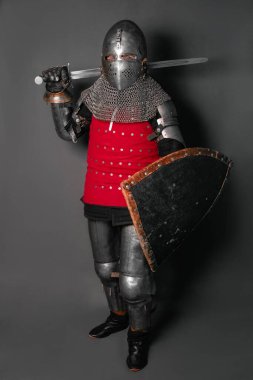 Zırhlı ve elinde kılıç olan bir ortaçağ şövalyesi savaş pozisyonunda duruyor ve silahını sallıyor..