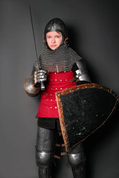 中世の鎧を着た若い騎士で剣と盾が灰色の背景に立っています — ストック写真