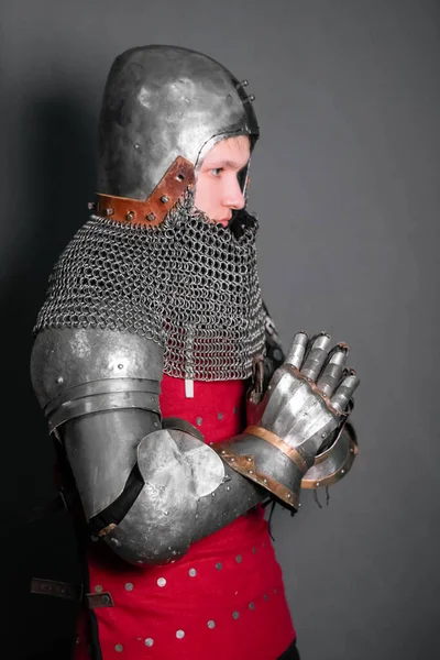 A young knight in medieval armor prays with his hands clasped.