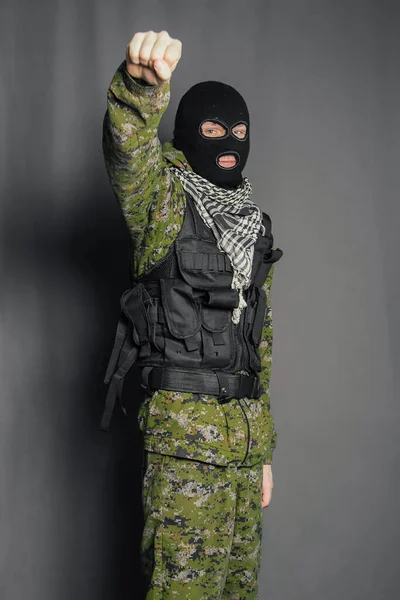 A man in camouflage and bullet proof vest, with a balaclava on his head. A special unit soldier, a modern warrior. A photo on a gray background, studio.