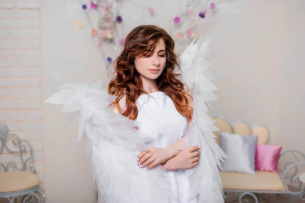 Portrait of a young woman, an angel in a white dress stands wrapped in wings.