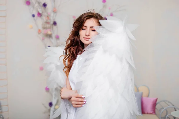 一个穿着白衣的天使站在用翅膀包裹着的年轻女子的画像 — 图库照片