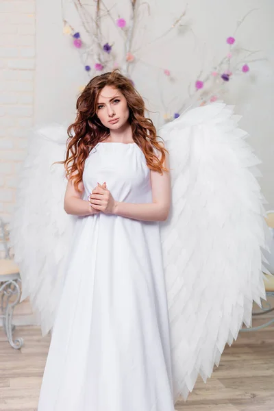 Portrait of a woman angel girl in a white dress with wings behind her folded hands in prayer.