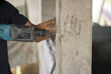 İşçi görüntüsü beton sütunu delmek için elektrikli matkap kullanıyor.