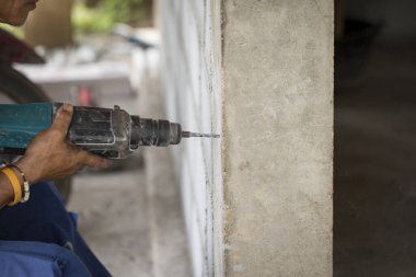 İşçi görüntüsü beton sütunu delmek için elektrikli matkap kullanıyor.