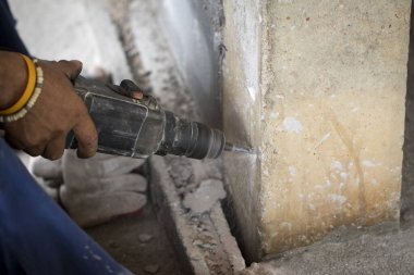 İşçi görüntüsü beton sütunu delmek için elektrikli matkap kullanıyor.