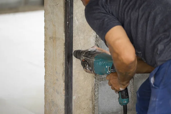 Image of worker using electric drill to drill the concrete pillar.