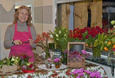 Pembe önlük mutlu orta yaşlı kadın çiçekçi buketler çiçek kendi dükkanında düzenler.