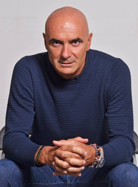 serious bald middle aged man sitting and looking at camera on grey background