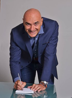 bald middle aged businessman writing in notebook and smiling at camera on grey background  