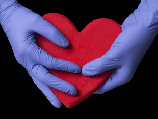 Doctor hands hold and protect a big heart on black background.