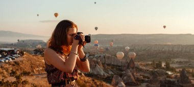 Kapadokya 'da gündoğumunda elinde kamerayla ve sıcak hava balonlarıyla uçan genç ve güzel bir kız fotoğrafçı. Goreme, Kapadokya, Türkiye. Pankart