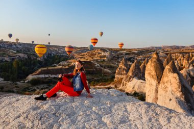 CAPPADOCIA, TURKEY 23 AĞUSTOS 2019: Kapadokya 'da gün doğumunda elinde kamera ve sıcak hava balonu uçuşuyla genç ve güzel bir kız fotoğrafçı. Goreme, Kapadokya, Türkiye