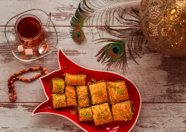 土耳其传统的甜点烘焙在盘子里 其形式是在桌上放郁金香茶 孔雀羽毛 念珠和装饰灯 场深度浅的照片 — 图库照片