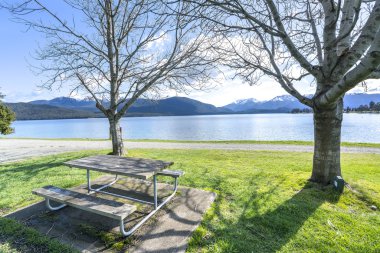 Te Anau, Yeni Zelanda'da göl manzarasına bakan ahşap masa ve sandalye