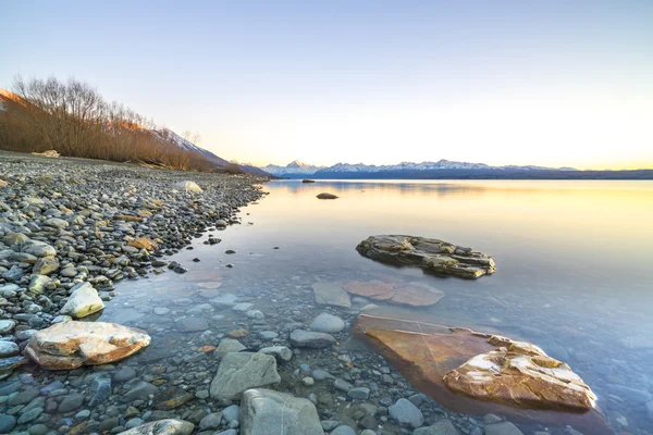 Камень у озера во время восхода солнца — стоковое фото