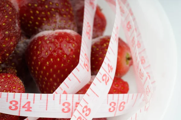 Frozen strawberries with tape measurement with white background. Diet concept.