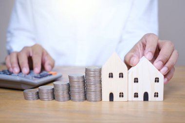 Ahşap ev modelinin yanına bozuk para istifle ve hesap makinesini kullanarak ahşap masada hesap yap. Gelecek yatırımlar için para biriktirmek ve ev almak için para biriktirmek..