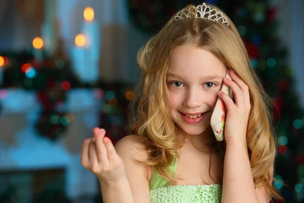 魅力的なかなり金髪子 美少女新年のツリーの背景に彼女の携帯電話で緑のドレスでの肖像画 — ストック写真