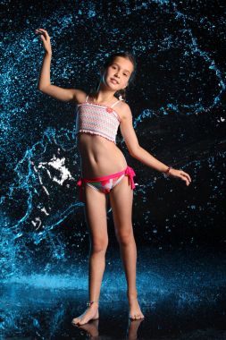 Sevimli genç genç kız bir mayo su sıçramasına yalınayak duruyor. Siyah saçlı, güzel yüz ve ince bir rakam ile güzel çocuk. İnce varoluş bir bikini.