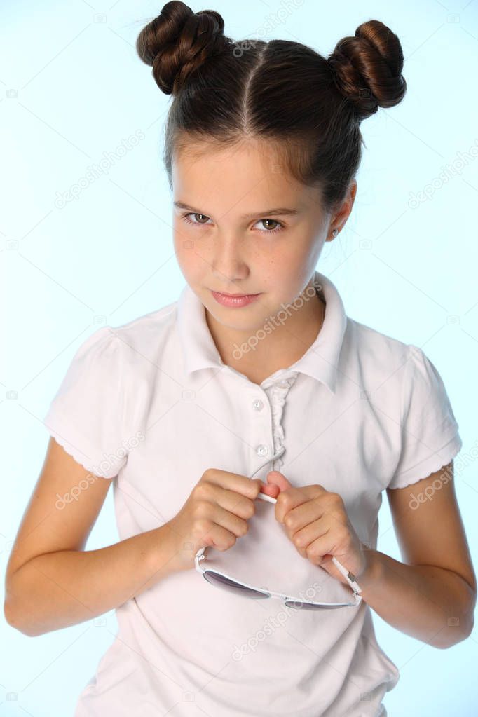 Portrait of a charming pretty stylish young teenage schoolgirl. Beautiful brunette child looks in disbelief. The little girl 12 years old in a white blouse with hairstyle.