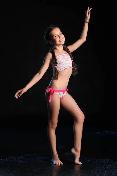 Tam vücut üzerinde sessizce ayakta ve gülümseyen sevimli ince çocuk. Genç ve güzel güzel mutlu kız zarif parlak bikinili poz çıplak ayaklı. Çekici genç genç siyah bir zemin üzerine